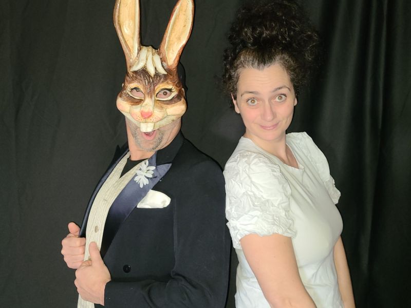 Alice au Pays des merveilles : un personnage au masque de lapin blanc, en costume, dos à dos avec une comédienne en robe blanche.