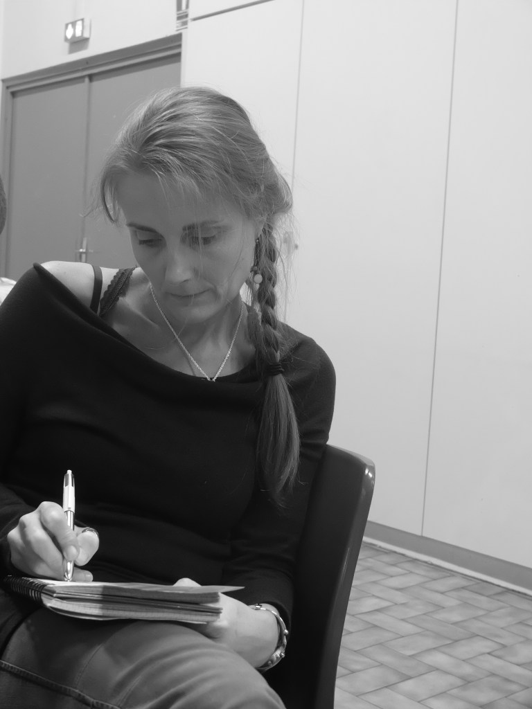 Portrait en noir et blanc d’Hélène Soubité, assise, une tresse sur l’épaule, en train d’écrire sur une tablette